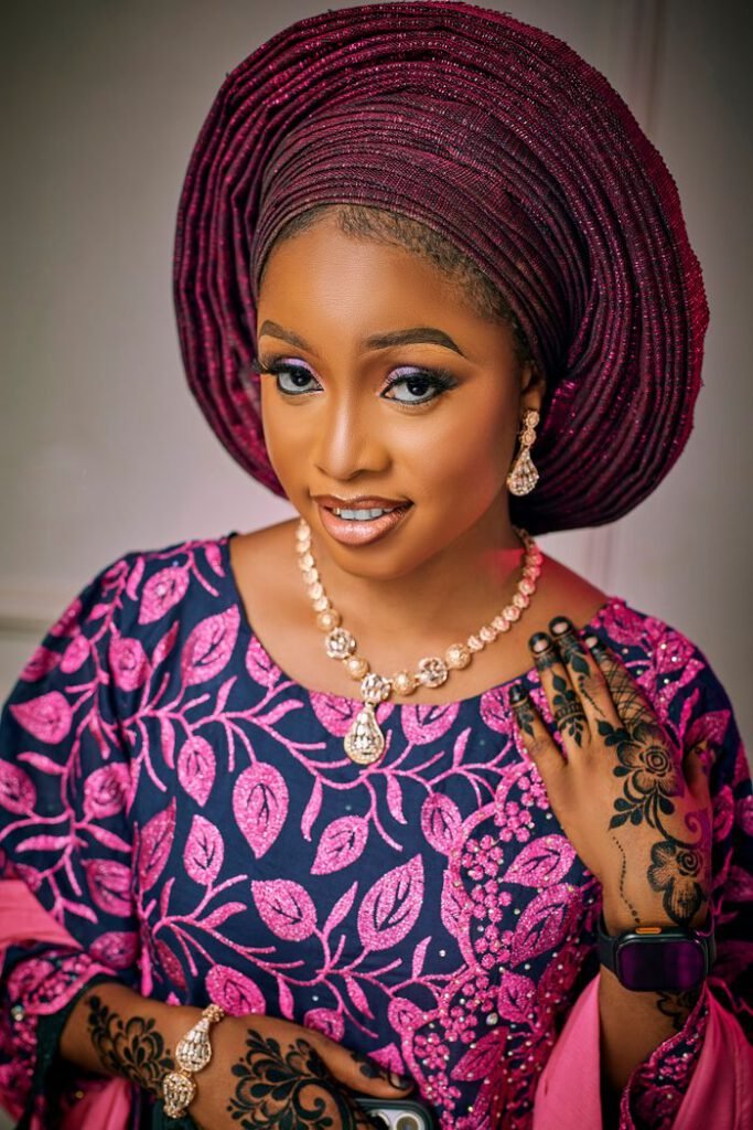 pexels photo 31848944 Smiling woman in pink and blue Aso Oke with jewelry and henna designs.