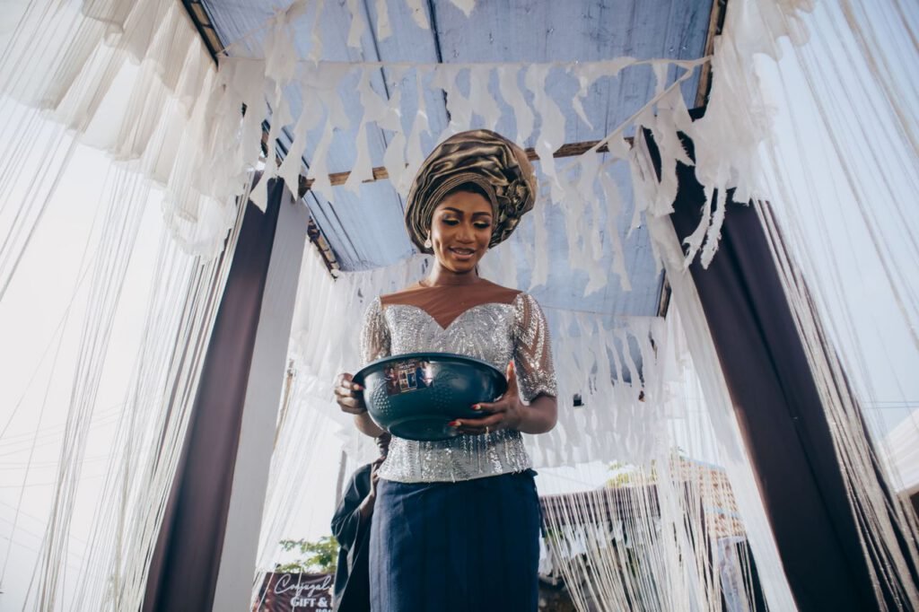 pexels photo 37080860 African woman in traditional attire holding a bowl during a cultural ceremony with decorative curtains.